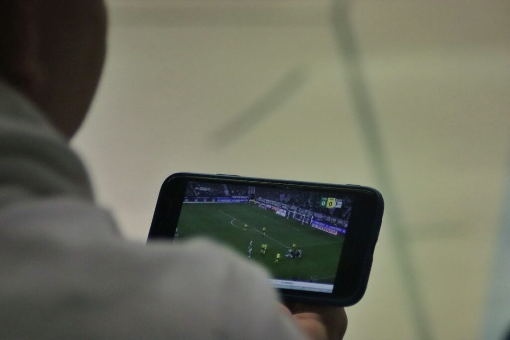 Pessoa usando celular durante partida de futebol