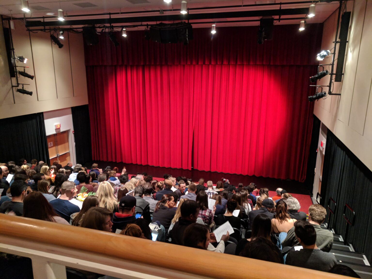 Plateia diante de palco de teatro com cortina vermelha